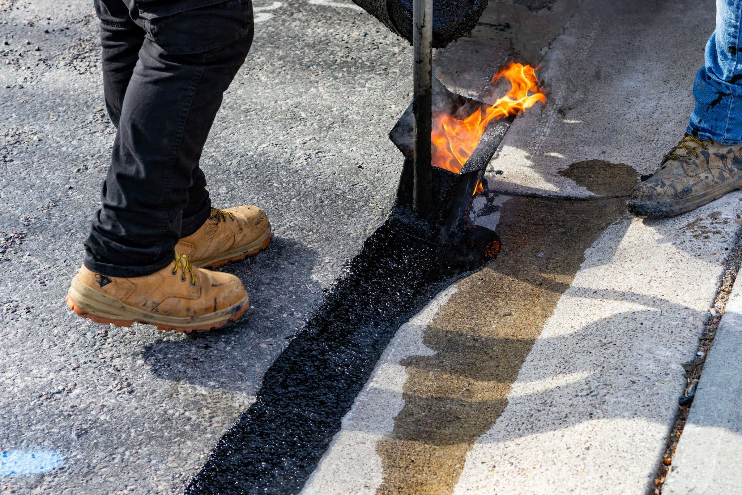 Two workers wearing work boots while repairing an asphalt road