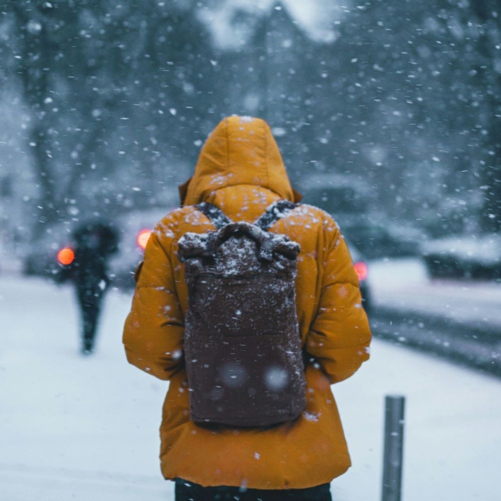 Person wearing warm winter clothing and carrying a backpack while walking through snow