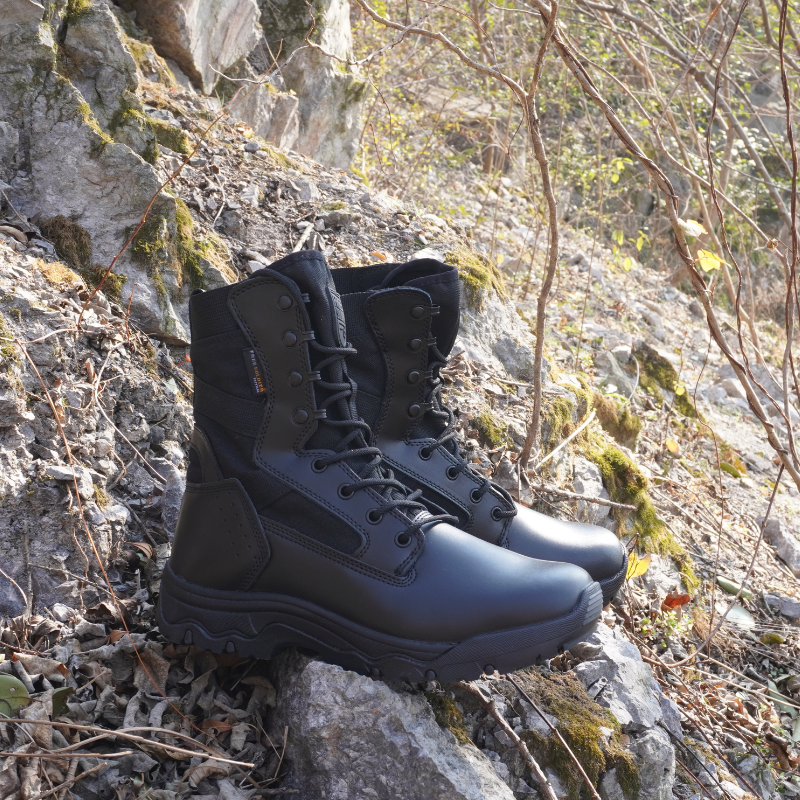 Black tactical combat boots with waterproof leather and Cordura upper, non-slip sole, and reinforced ankle support, positioned outdoors on rocky terrain – ideal for military, hiking, and rugged outdoor work